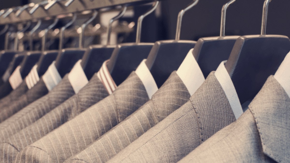 A row of neatly hung suits in various shades of grey on hangers, displayed on a metal rack in a clothing store.