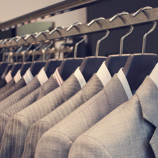 A row of neatly hung suits in various shades of grey on hangers, displayed on a metal rack in a clothing store.