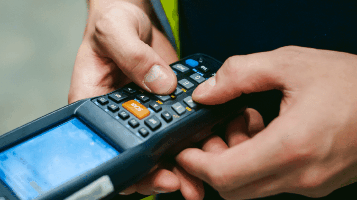 A person in a high-visibility vest operates a handheld barcode scanner, highlighting their hands and device—an essential tool during WMS implementation for efficient inventory management.