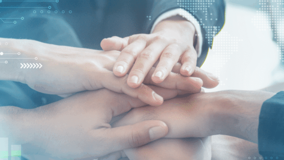 Several people stack their hands together in a gesture of teamwork and unity, with digital graphics of world maps and bar charts overlaying the image, suggesting global business collaboration.
