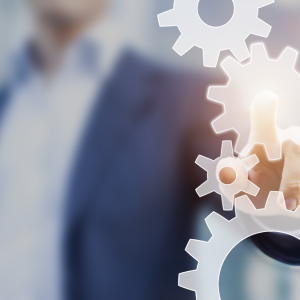 A person in a suit touches a glowing gear icon on a transparent screen, symbolizing technology, innovation, or process management.