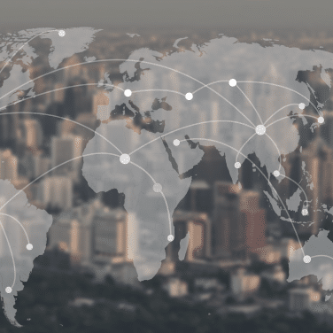 A world map with connected nodes is overlaid on a blurred cityscape, symbolizing global communication and networking. White lines link multiple points across continents.