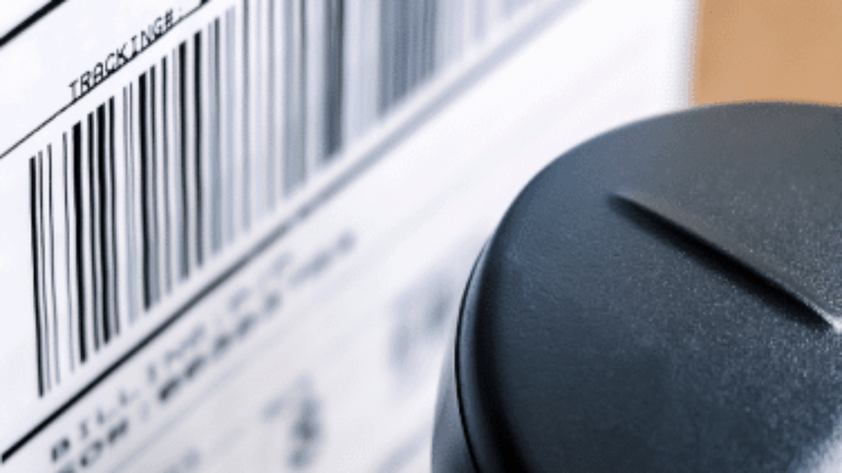 Close-up of a barcode and tracking label on a package, with part of a black handheld barcode scanner in the foreground.