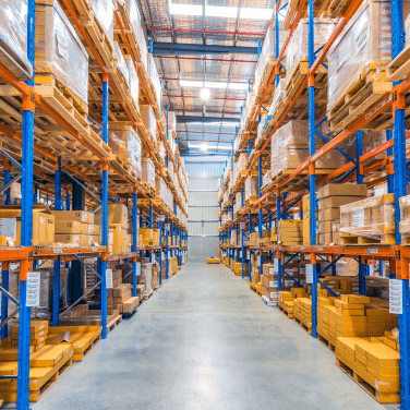 A brightly lit warehouse with tall shelves stacked with neatly organized boxes and packages, creating clear aisles for easy access—showcasing what slotting can achieve in maximizing storage efficiency and workflow.