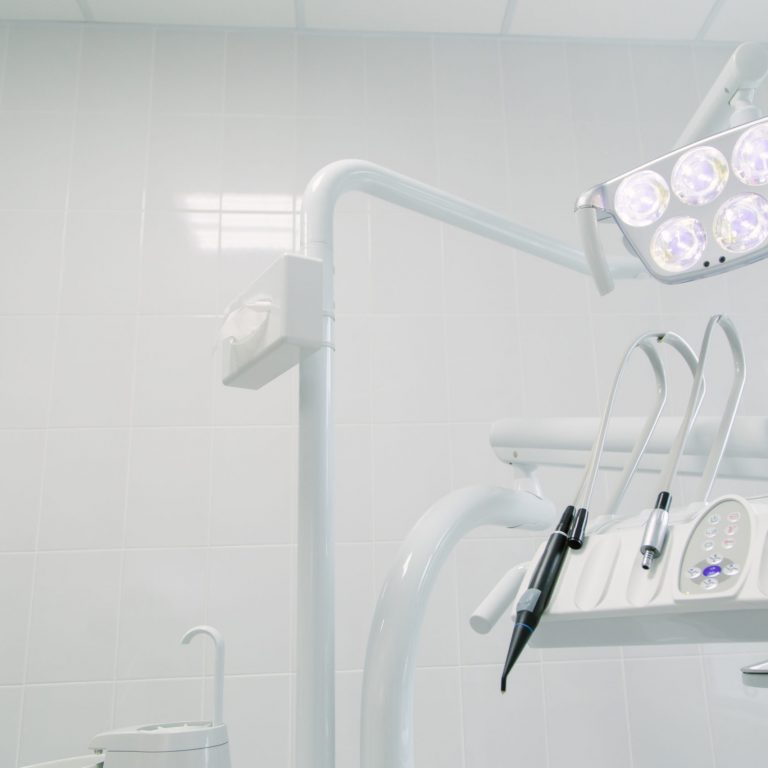 Modern dental office with bright overhead lights, dental instruments, and a clean white tiled wall, showcasing a sterile and organized environment for dental procedures.