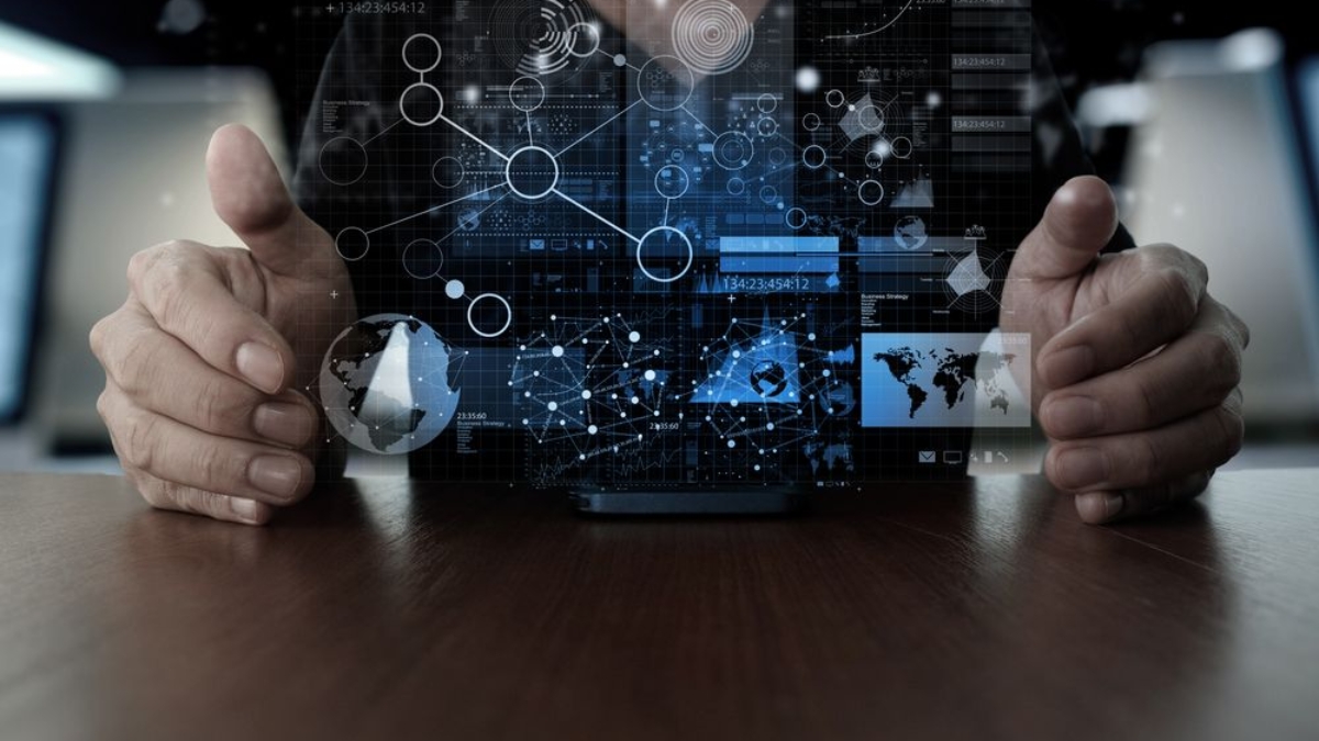 Person holding hands around a table with a digital interface of futuristic graphs, data charts, and network connections projected in the air above a mobile device.