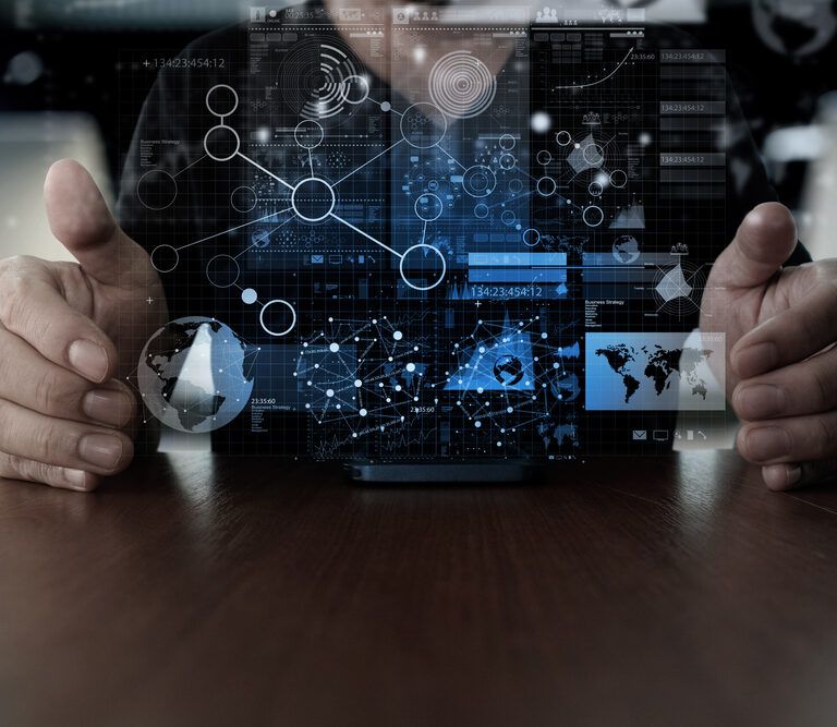 Person holding hands around a table with a digital interface of futuristic graphs, data charts, and network connections projected in the air above a mobile device.