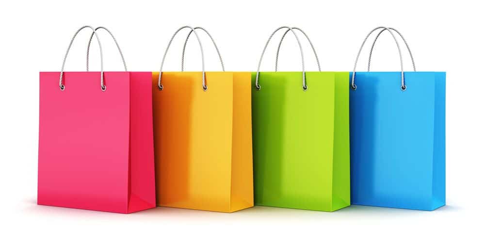 Four shopping bags in bright colors—red, yellow, green, and blue—stand side by side with silver handles against a white background, showcasing a vibrant merchandising strategy.
