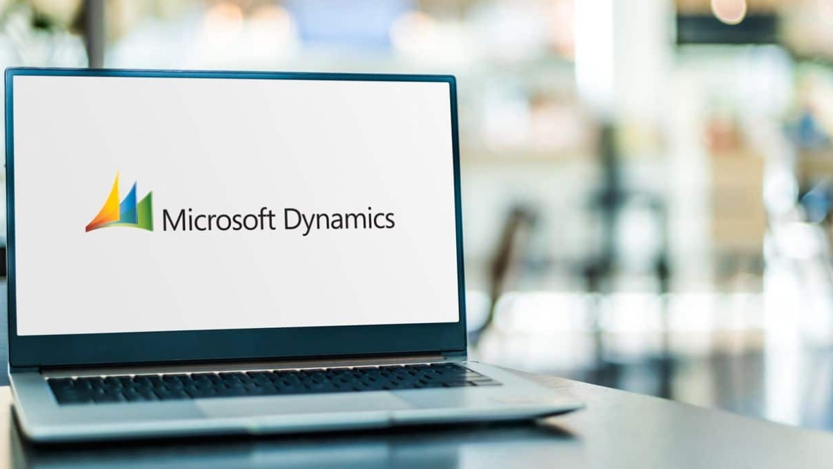 A laptop on a table displays the Microsoft Dynamics logo on its screen. The background is blurred, suggesting an office or workspace environment.