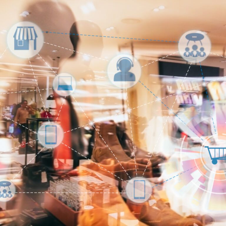 A blurred clothing store interior with digital icons—shopping cart, store, smartphone, and people—connected by lines to represent online shopping, digital retail technology, and enhanced inventory visibility.