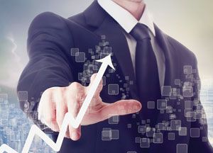 A man in a suit touches a virtual upward-pointing graph, symbolizing business growth or successful supply chain cost management, with digital square icons floating around his hand.