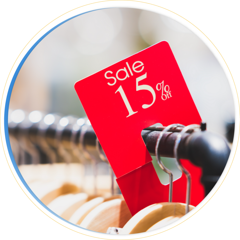 A red sale sign showing 15% off is attached to a clothing rack with wooden hangers, highlighting a pricing promotion on the items for sale.