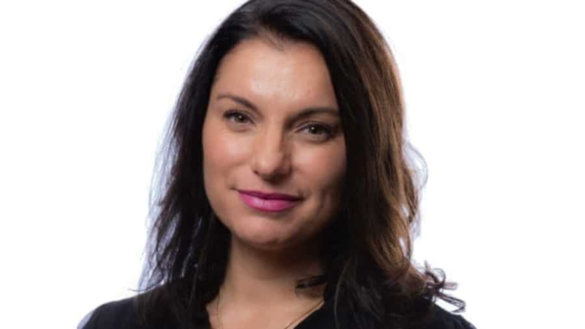 A woman with long dark hair and a slight smile, wearing a black top, is pictured against a plain white background.