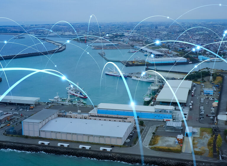 Aerial view of a busy port with warehouses, ships, and blue water. Digital lines and glowing points are overlaid, symbolizing a responsive supply chain with seamless network connectivity and efficient data transfer across the port.