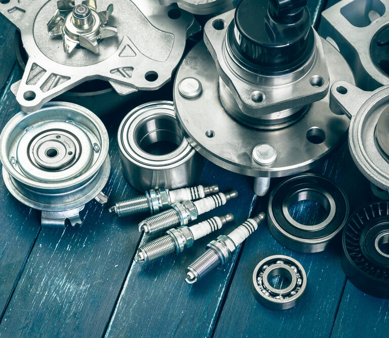 Various metal car engine parts, including spark plugs, bearings, and gears, are arranged on a blue wooden surface. The image highlights the details and textures of the automotive components.
