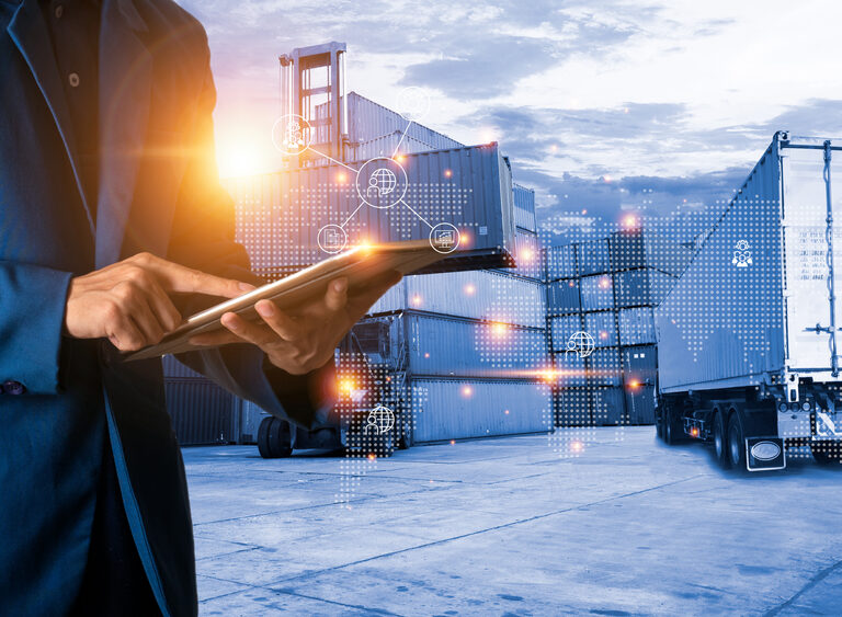 A person in a suit uses a tablet at a shipping yard with stacked cargo containers and a truck. Digital network graphics overlay the scene, highlighting advanced supply chain planning and logistics technology.