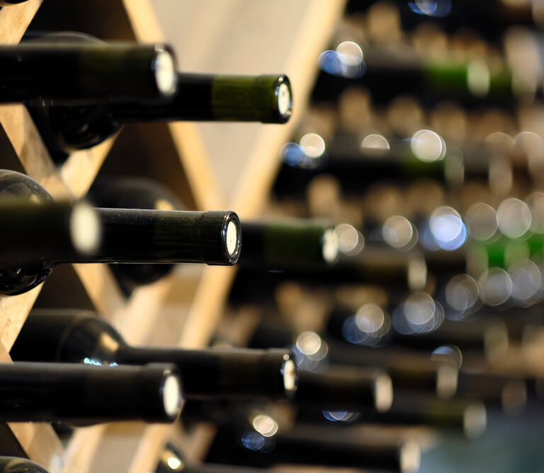 Several wine bottles stored horizontally on wooden racks, with bottle necks facing outward and the background softly blurred, giving a sense of depth and focus on the wine storage.