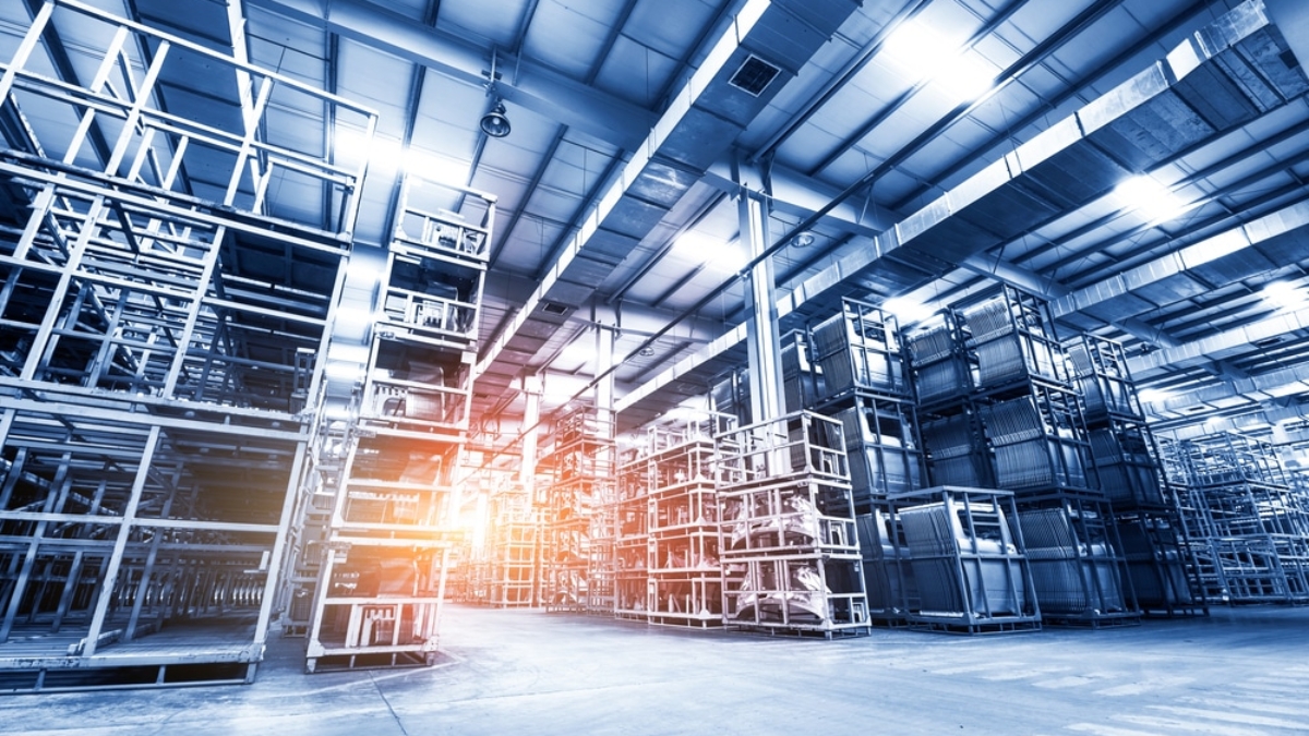 Large, modern warehouse interior with tall, empty metal shelving units and a high ceiling. Sunlight streams in from the left, highlighting the spacious industrial atmosphere—ideal for implementing slam line automation systems.