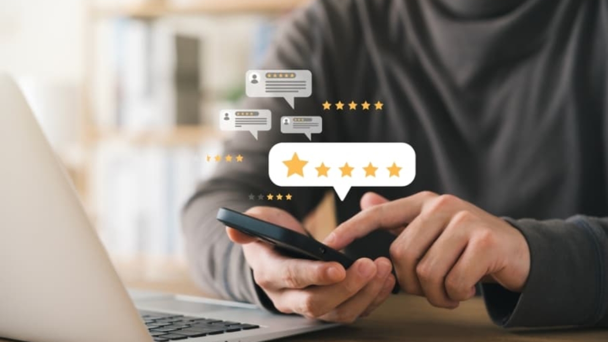 A person sits at a desk using a smartphone next to a laptop, with illustrated five-star rating and review icons floating above, suggesting online feedback or customer review activity powered by Microsoft Dynamics 365 Customer Experience.
