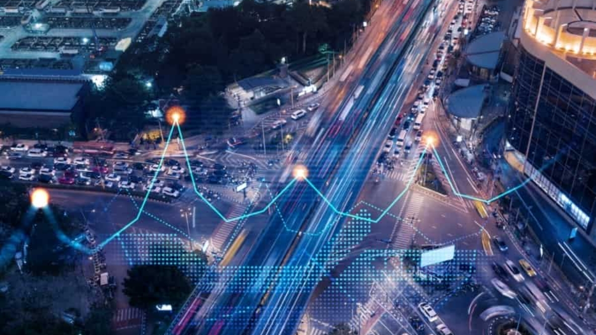 Aerial view of a busy city intersection at night with light trails from moving vehicles. A digital graph line overlays the road, symbolizing data analysis or smart city Supply Chain Technology Selection.