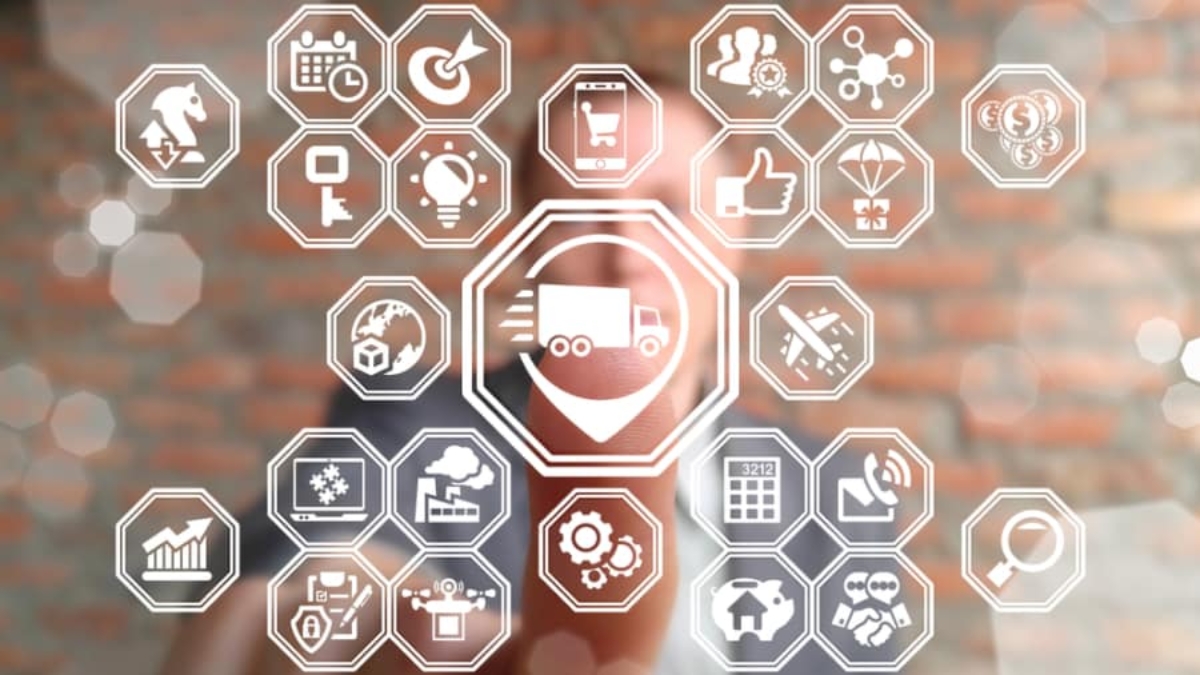 A person interacts with a transparent digital interface displaying various octagonal business and logistics icons, including a central truck symbol, graphs, gears, a calendar, and communication symbols, against a blurred brick wall background.