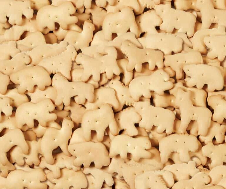 A pile of assorted animal-shaped cookies, known as animal crackers, featuring various animal designs in light golden brown color.