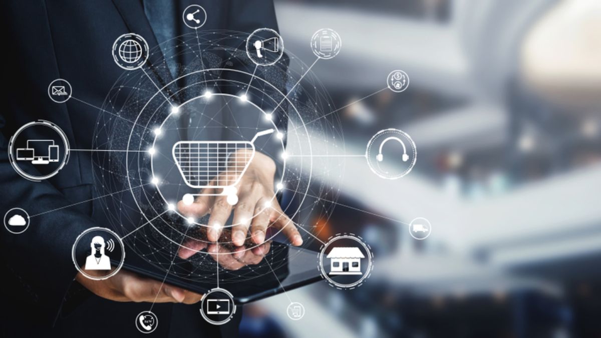 A person in a suit uses a tablet, with digital icons related to online shopping, technology, and communications floating above, symbolizing e-commerce and digital marketing concepts.