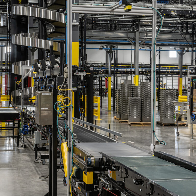 Busy warehouse interior with conveyor belts, stacked cardboard boxes, metal shelves, automated machinery, and organized workstations, powered by SLAM solutions for an industrial and highly automated environment.
