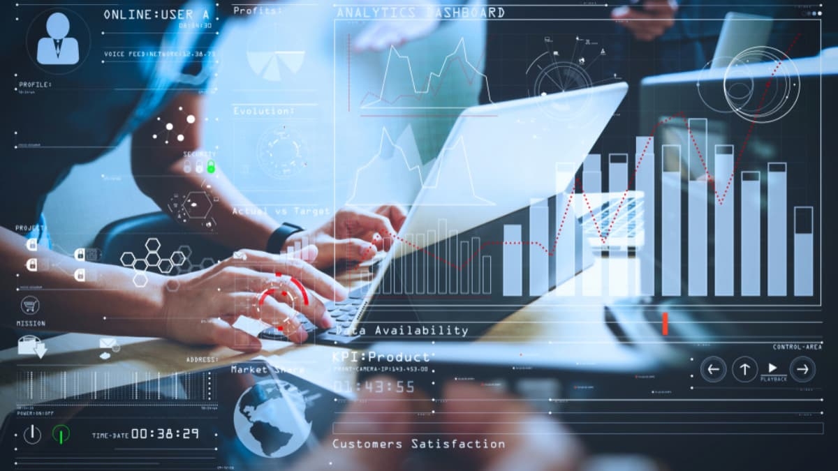 People working on laptops at a desk overlaid with digital graphs, charts, and data analytics visuals, representing teamwork, technology, and business data analysis.