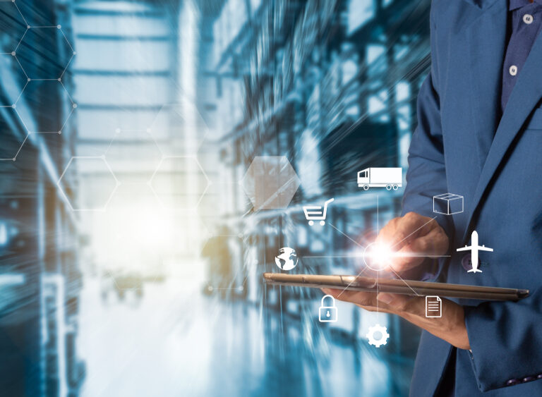 A person in a suit uses a tablet, with logistics and supply chain icons like a truck, cart, box, airplane, and lock overlaid. The background shows a blurred warehouse or industrial setting.