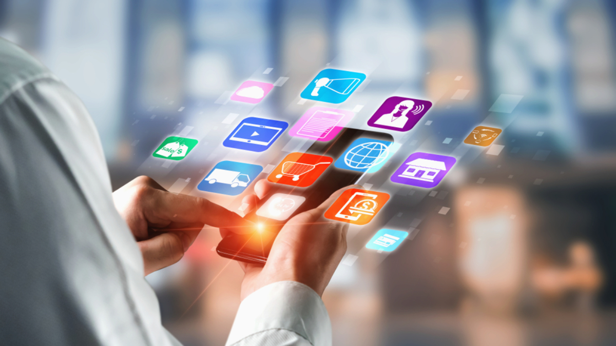 A person uses a smartphone with colorful app icons, including artificial intelligence services, floating above the screen, symbolizing various digital and online services. The blurred background highlights the focus on mobile technology.