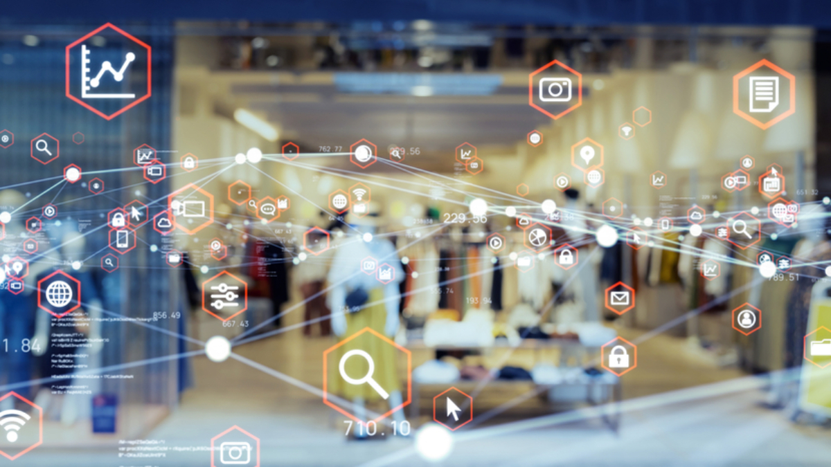 A clothing store interior is visible through a glass window overlaid with digital icons like graphs and shopping carts, symbolizing retail technology and data integration—key elements in understanding what is supply chain strategy today.