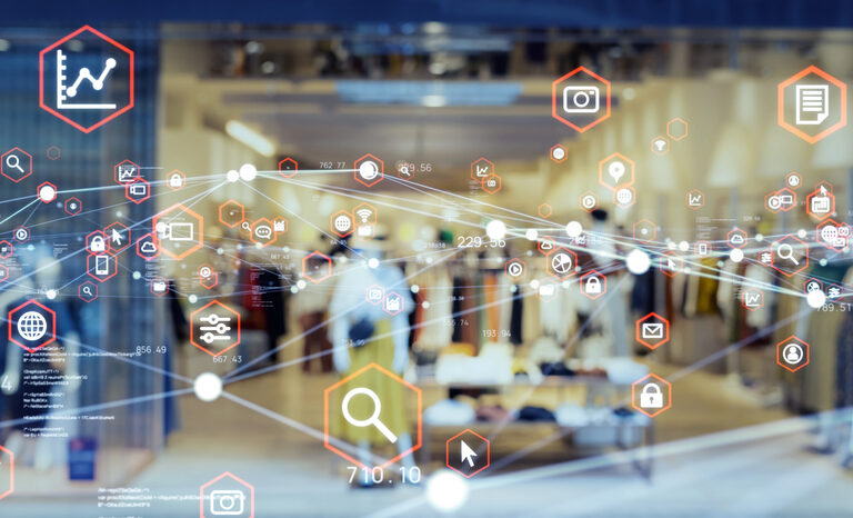 A clothing store interior is visible through a glass window overlaid with digital icons like graphs and shopping carts, symbolizing retail technology and data integration—key elements in understanding what is supply chain strategy today.