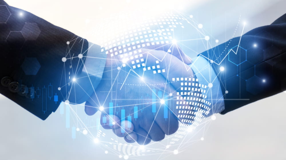 Two people in business suits shaking hands, with a digital globe and network-style graphics overlayed, symbolizing global business, partnership, and technology.