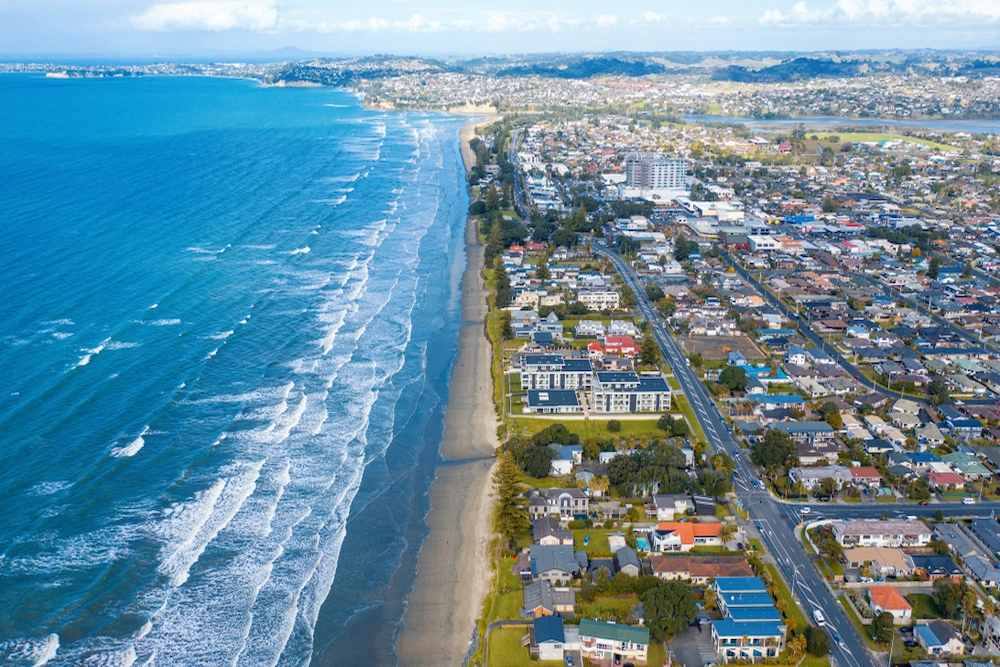 Aerial view of a coastal city with waves crashing on a sandy beach, residential houses, roads, and urban buildings stretching along the shoreline under a partly cloudy sky, ideal for those seeking enVista Careers in vibrant urban settings.