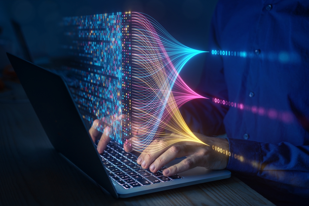 A person types on a laptop keyboard, with vibrant digital streams and binary code emerging from the screen, symbolizing data transfer, information technology, or enVista Careers in innovative fields like parcel audit service.