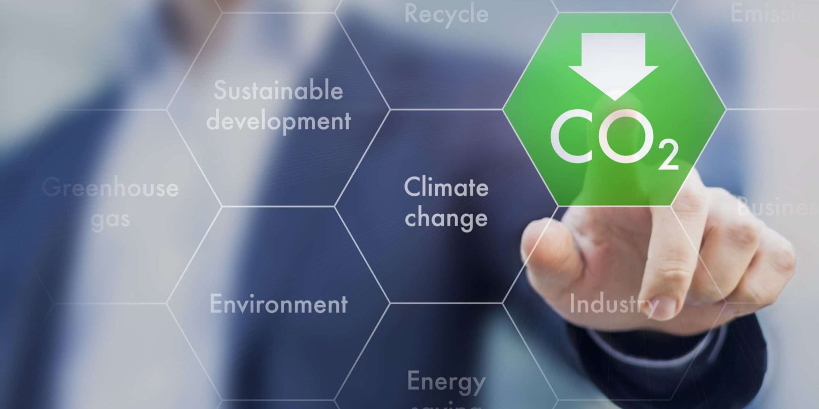 A person presses a digital hexagon labeled CO₂ with a downward arrow on a transparent screen. Surrounding hexagons display words like Climate change, Sustainable development, and Environment.