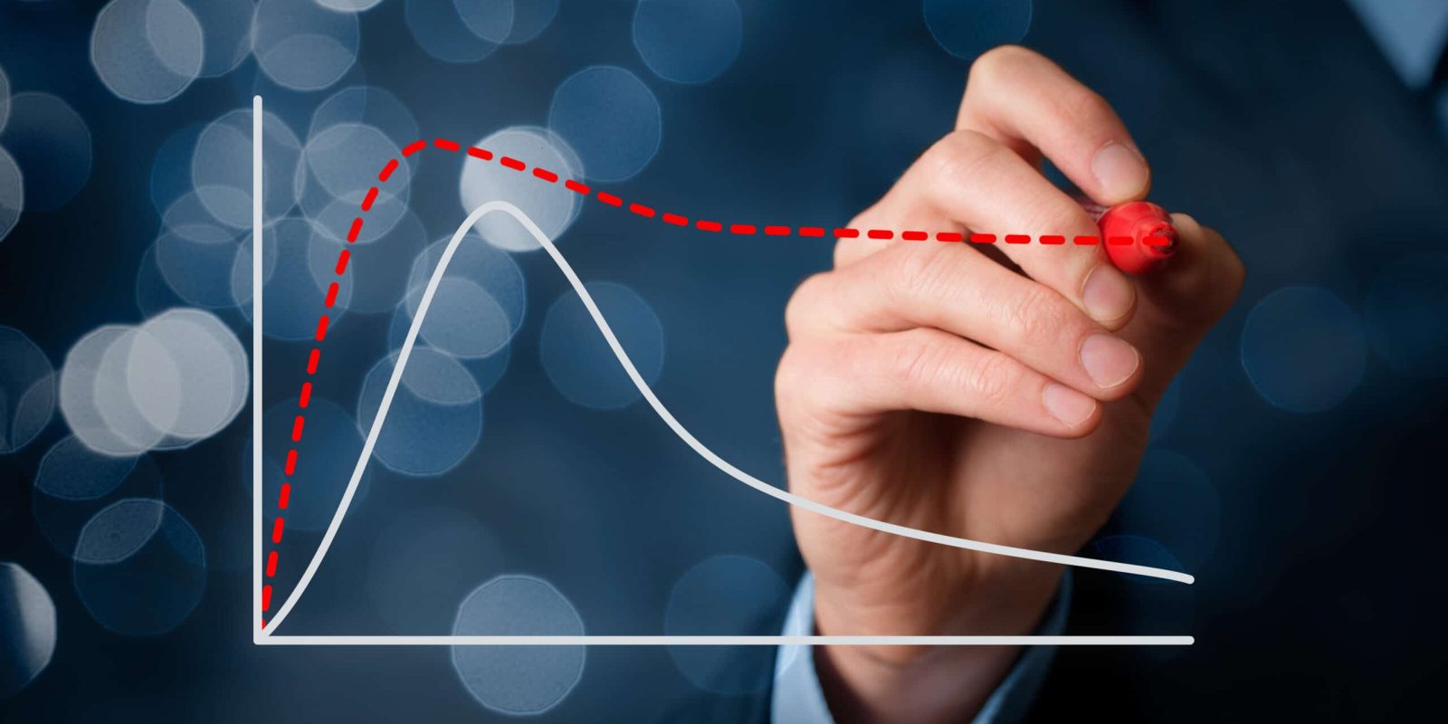 A hand in a suit draws a red dashed trend line above a white line graph on a transparent screen, with blurred blue lights in the background.